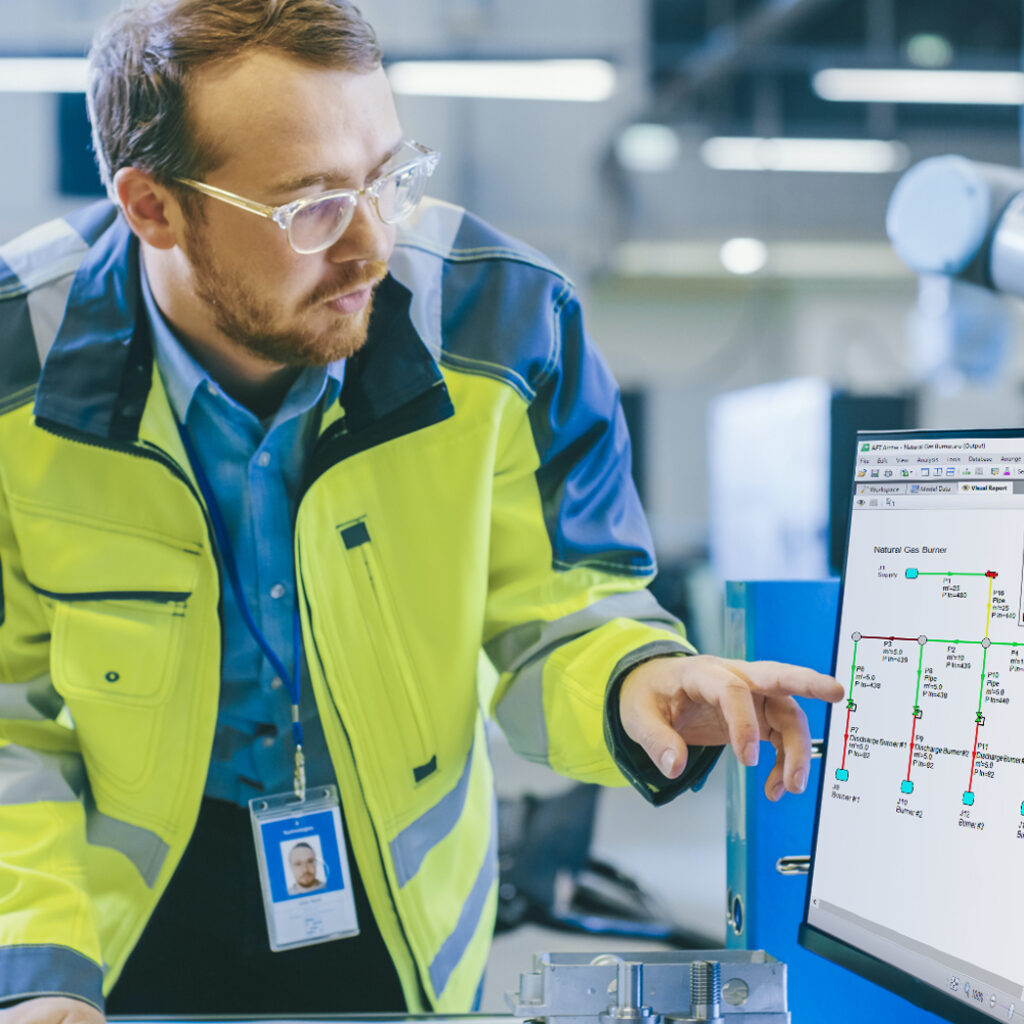 Man in a yellow security coat pointing at a plan on a computer.