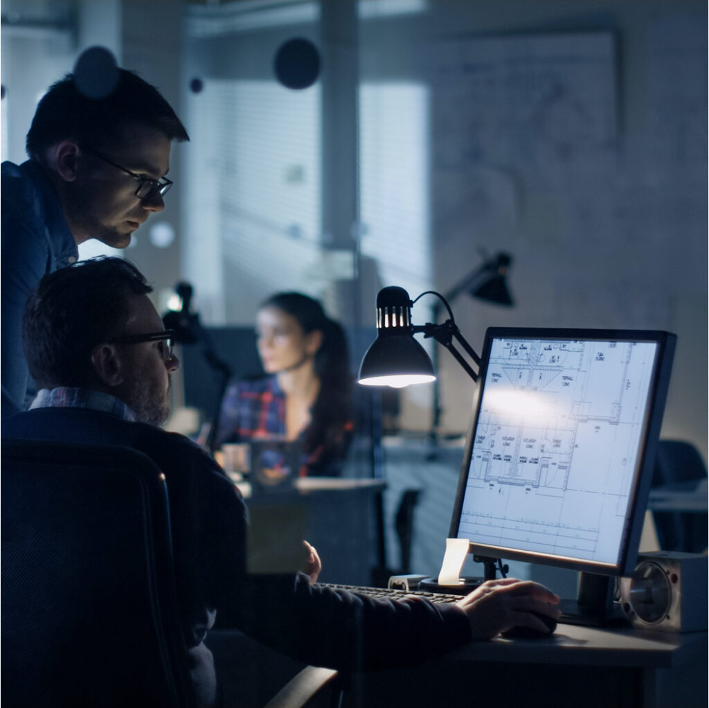 Two man in a dark office looking at a plan on a computer.